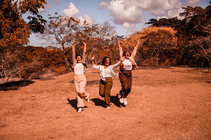 Três mulheres saltando e sorrindo em um ensaio ao ar livre