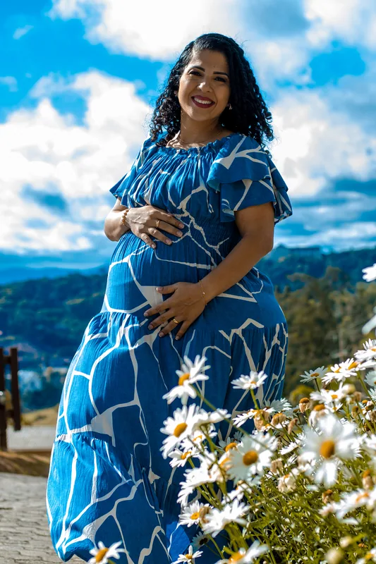 Gestante de vestido azul em um jardim com montanhas ao fundo