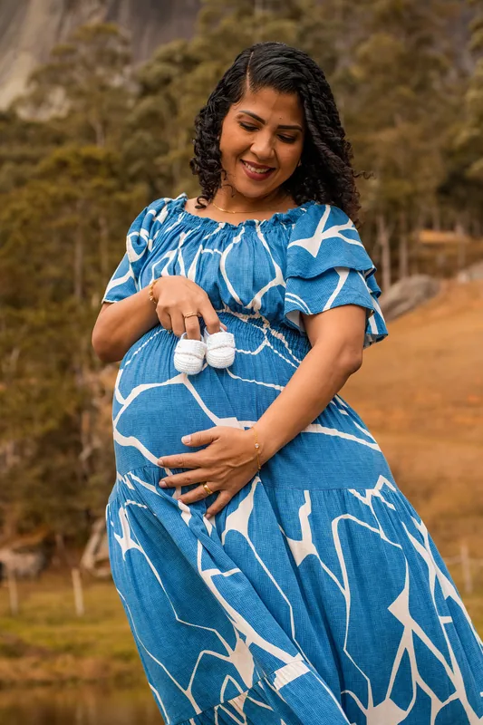 Gestante segurando sapatinhos sobre a barriga durante um ensaio ao ar livre